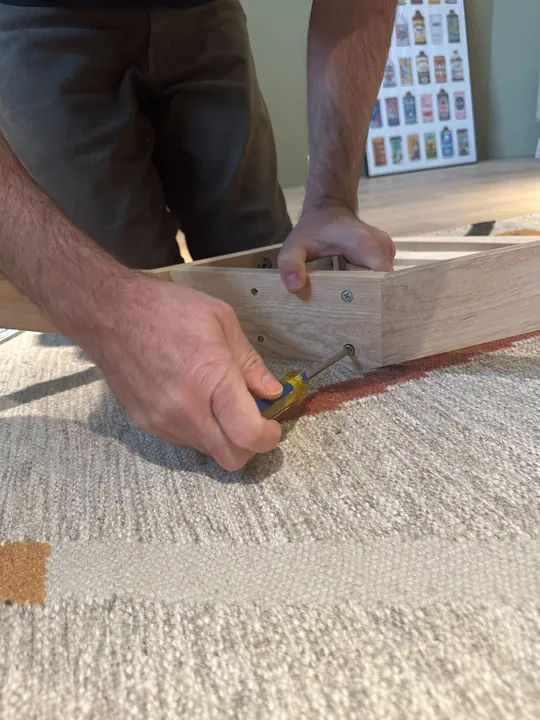 A close view of hands joining two maple stand legs with a screwdriver.
