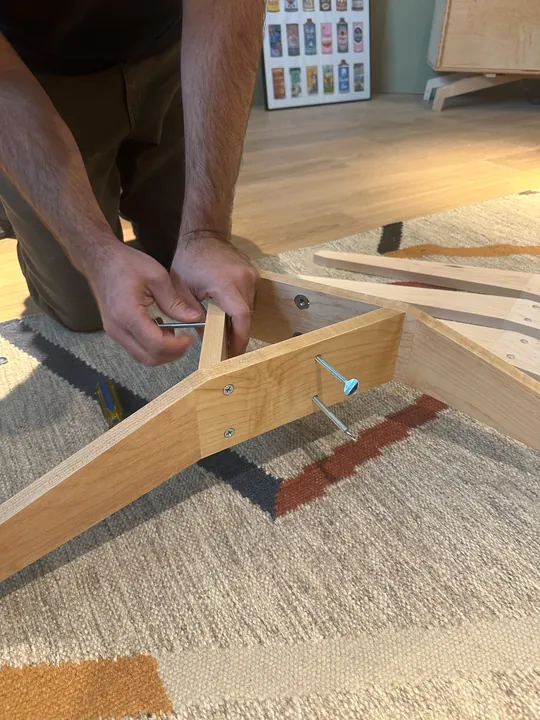 Hands using a screwdriver at a corner of the triangular maple stand.