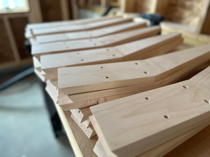 A row of shaped maple stand legs laid across the workshop bench.