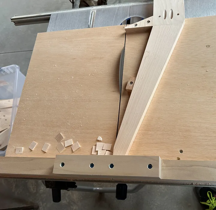 A maple stand leg in a wooden jig beside the table-saw blade.