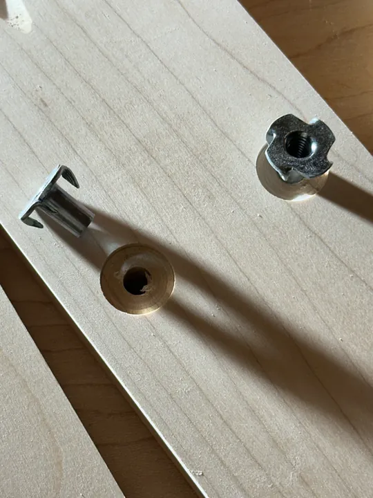 A drilled maple stand leg with a metal T-nut partly inserted and another T-nut beside it.