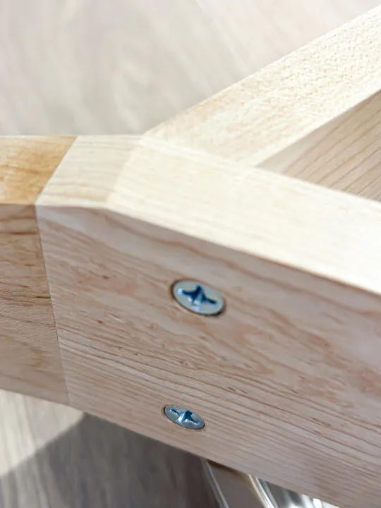 A close view of two maple stand legs meeting at a corner with wood screws visible.