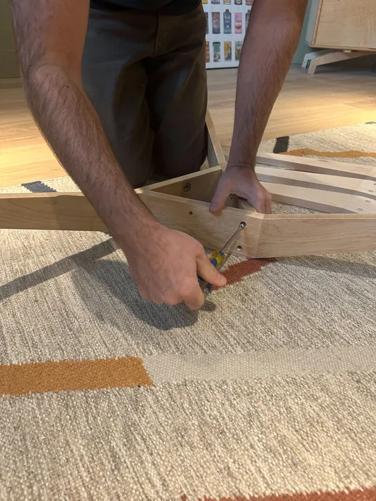 Hands holding two maple stand legs together while using a screwdriver at the joint.