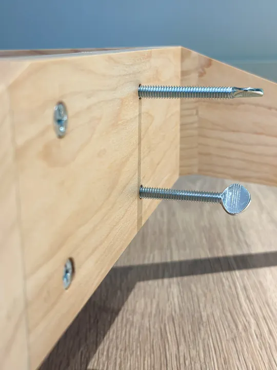 Two wood screws and two thumb screws in a maple stand corner, viewed from the side.