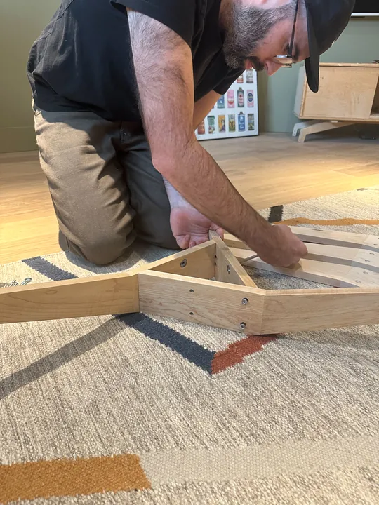 Jeremy fitting together the wooden stand on a rug.