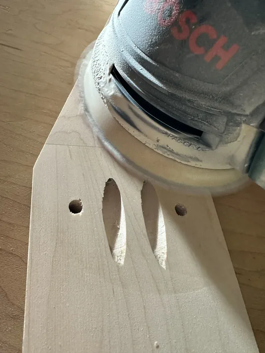 An orbital sander resting on drilled maple stand parts.